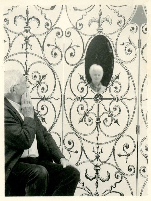 Black and white portrait of a man sitting against a patterned wall