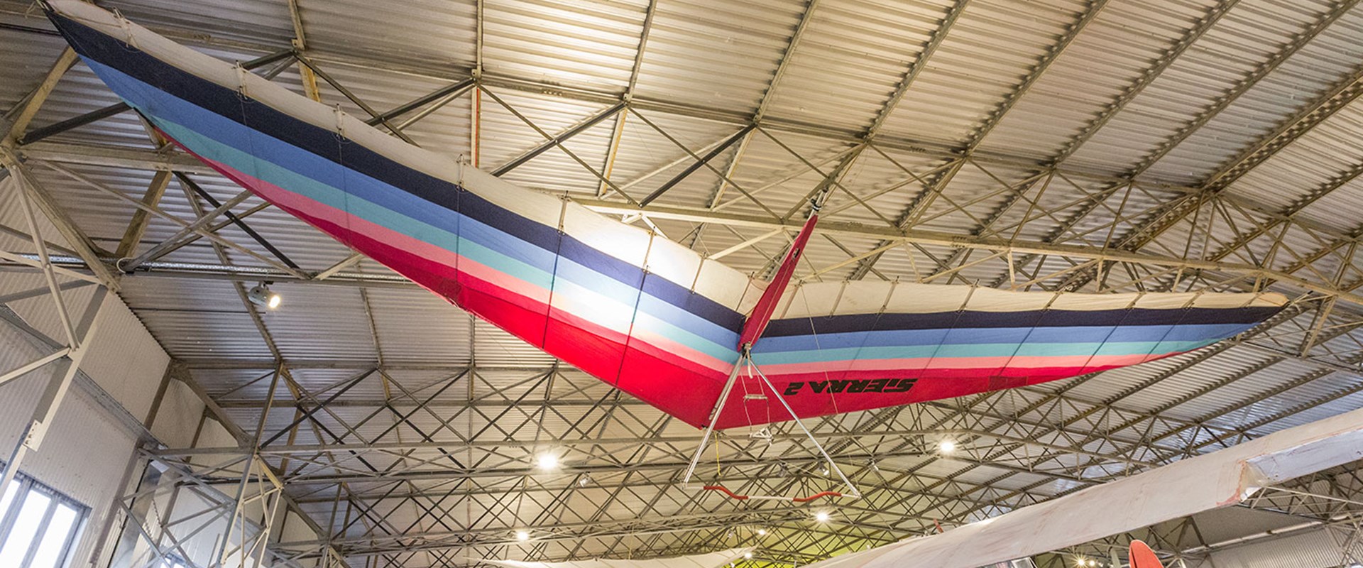 A mutlicoloured hang glider suspended from the ceiling of a hangar at the National Museum of Flight.