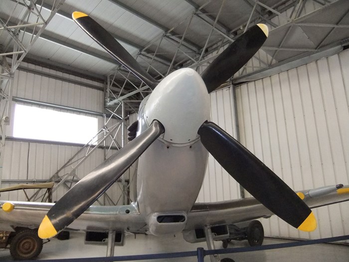 The nose and front propeller of a Supermarine Spitfire parked in a large aviation hangar.