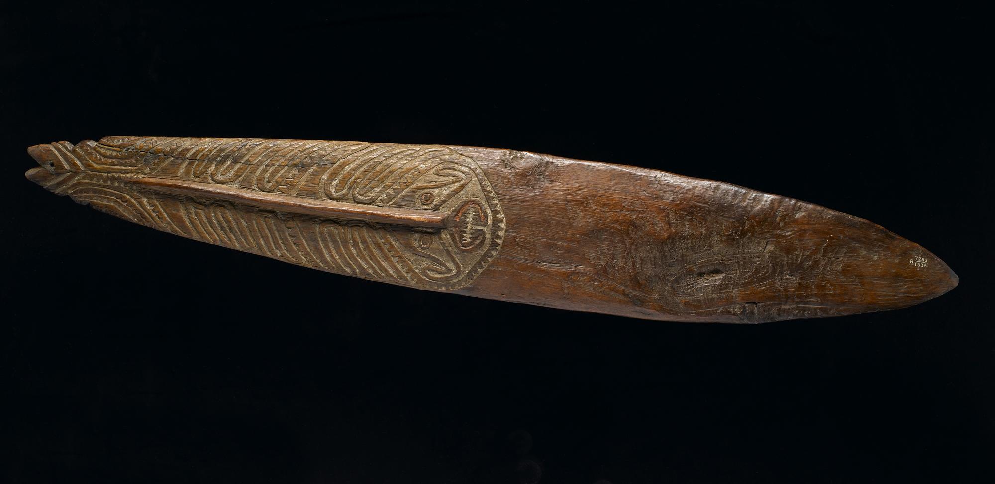 Bullroarer made of wood, carved with designs, including a human face, and decorated with pigment: Oceania, Melanesia, Papua New Guinea, Gulf Region, 19th century.
