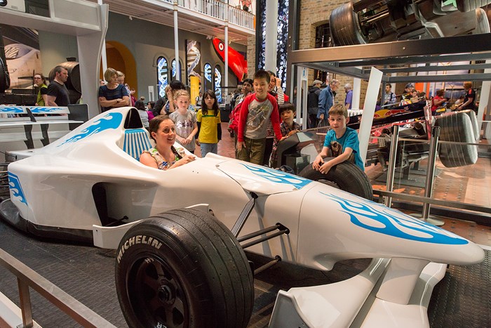A visitor sits in an F1 racing car, with a group of people watching on.