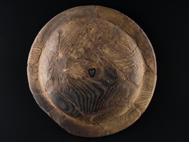 Wooden platter shaped like a round shield, slightly darkened at the bottom with a cartoon-like heart carved in the centre.