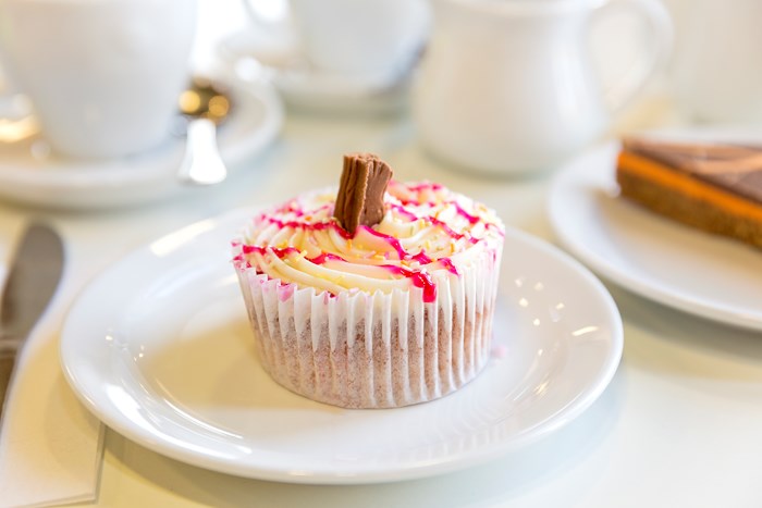 A cupcake with drizzle and a chocolate flake on a plate.