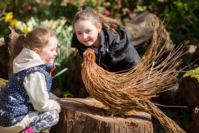 Two young children looking at a willow sculpture of a pheasant.