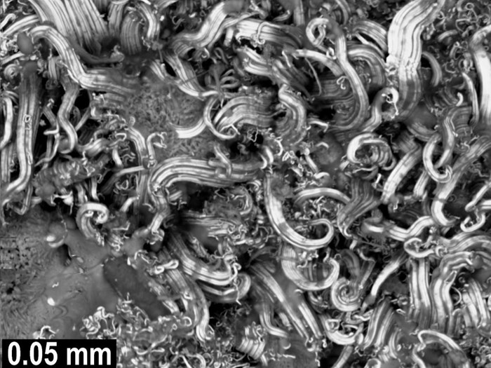 Extreme microscopic closeup of silver coils, folded together like waves in a turbulent ocean.