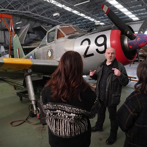 Two visitors listening to a man talking in front of an aircraft.
