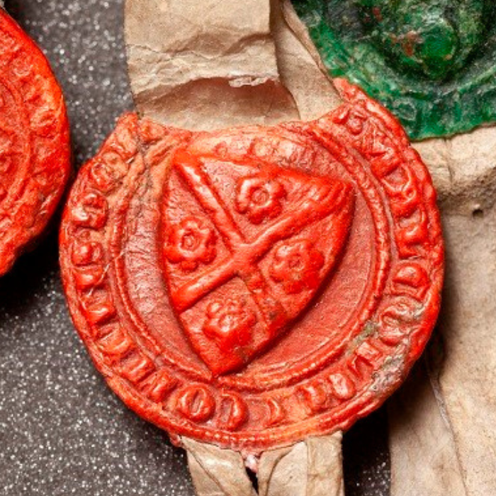 Closeup of a red wax seal from the Declaration of Arbroath. The seal has a coat of arms divided into four sections and Latin letters around its edge.