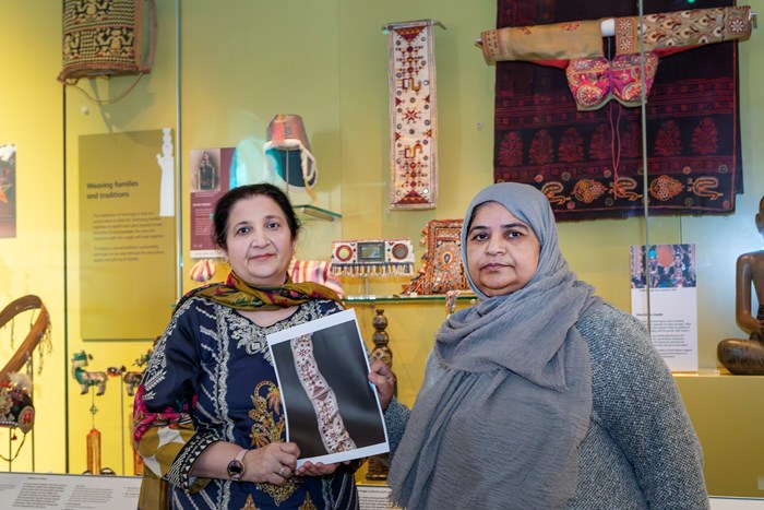 To women hold up a printed image of the scarf in the Performance and Lives gallery.