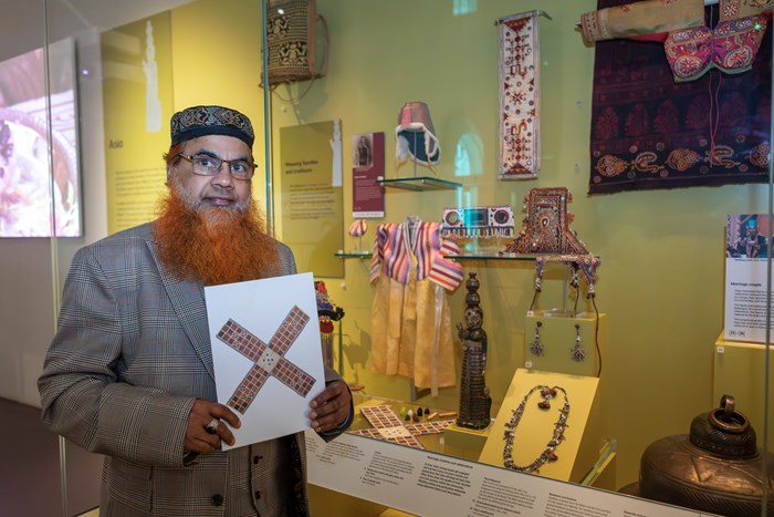 KS group member holds a picture of the chausur board in the Patterns of Life gallery.
