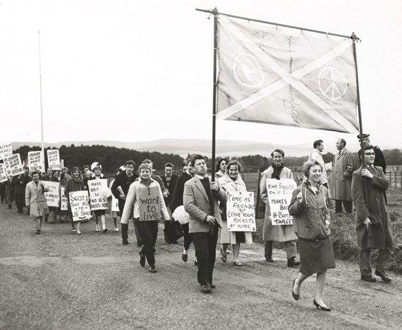 Black and white photo of a large group of young people walking and holding homemade signs with peaceful slogans.