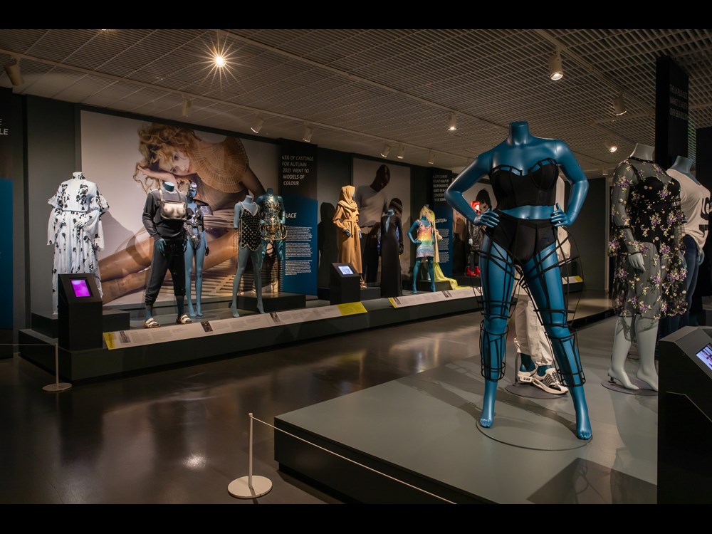 Thirteen mannequins arranged in exhibition, with blue blackdrops.