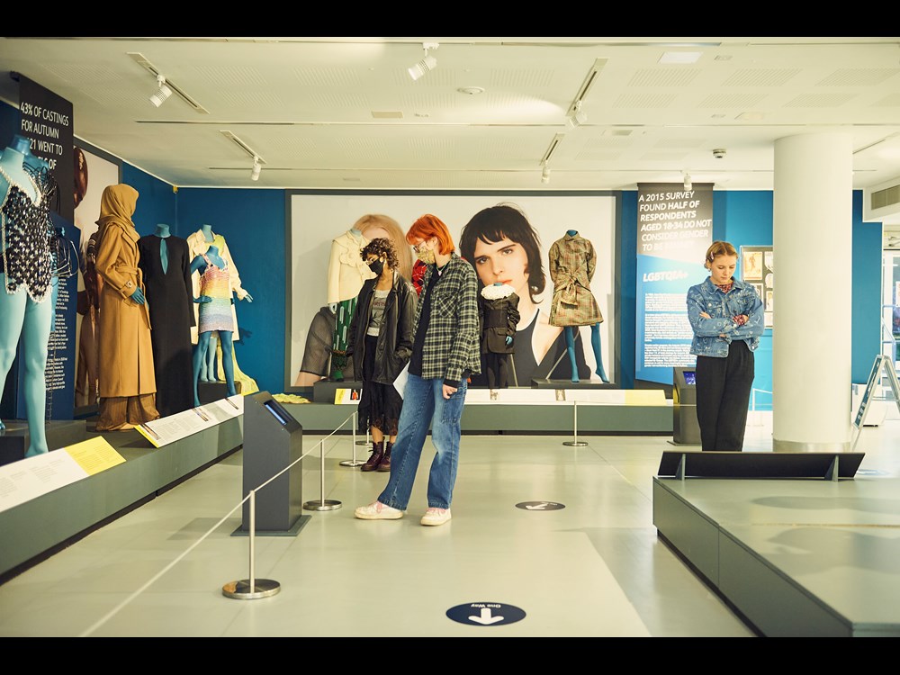 Three visitors in face-masks look at a selection of styled mannequins within the exhibition.