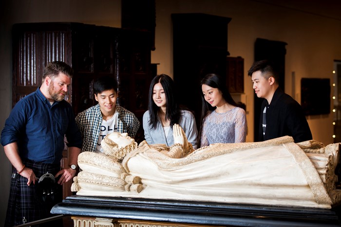 A group of five people look at a replica of the tomb of Mary, Queen of Scots.