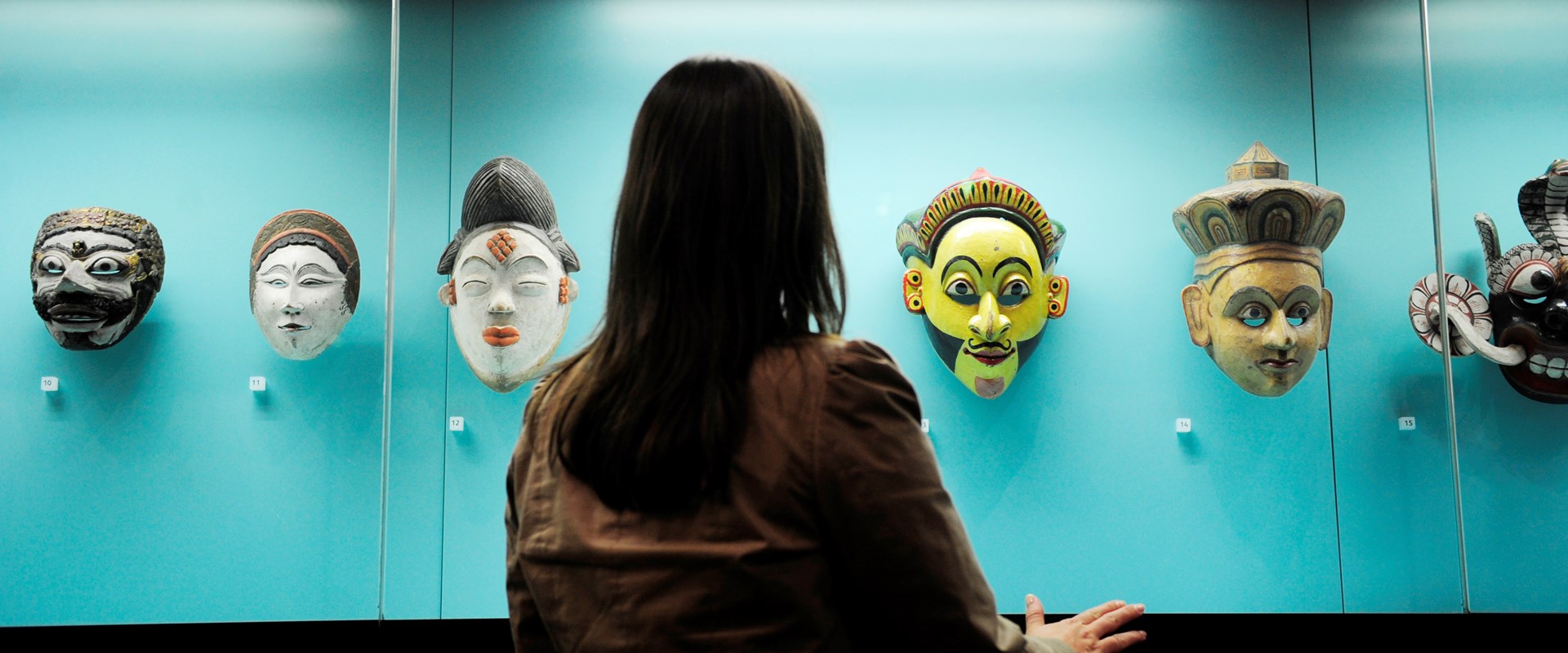 A woman viewing a series of costume masks in the Performance Lives gallery