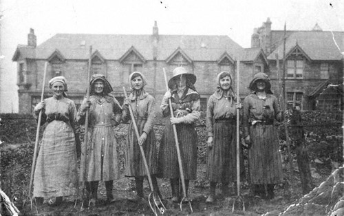 A black and white photograph of 6 women standing outside with pitchforks.