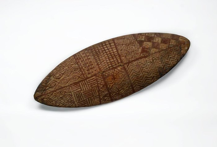 An aboriginal shield with carved patterns in the wood.