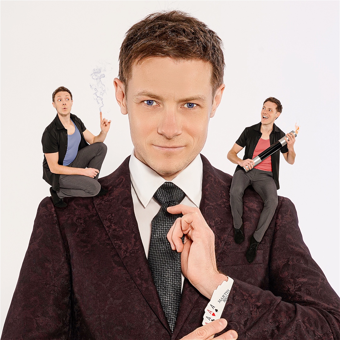 Martin Brock in a suit, flashing four Ace playing cards hidden up his left sleeve. There are two smaller versions of himself sitting on his shoulders, one with a magic wand, the other with a smoking finger gun.