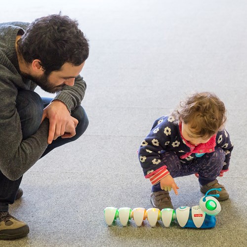 A parent and young child play with a toy robotic caterpillar 