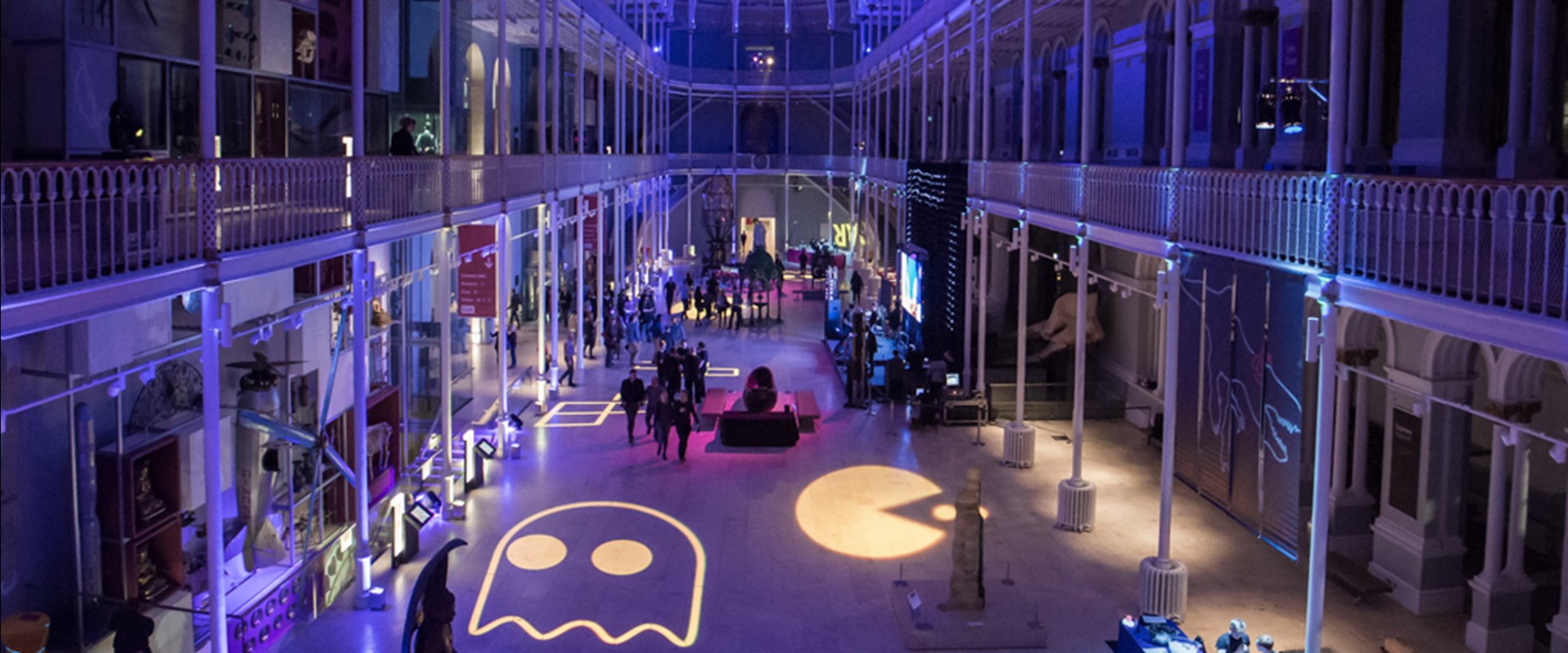 The Grand Gallery at night, with dark purple and pink lighting and activities across the floor. Gaming shapes are projected onto the floor too.